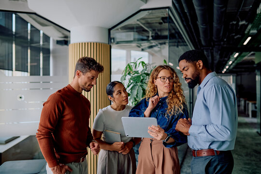 Diverse business team collaborating, discussing project on a tablet in a modern office, showing teamwork and problem-solving