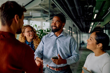 Diverse business team collaborating and shaking hands in an office hallway, fostering networking, inclusion, and a welcoming atmosphere