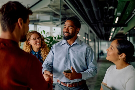 Diverse business team collaborating and shaking hands in an office hallway, fostering networking, inclusion, and a welcoming atmosphere - Powered by Adobe