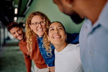 Diverse business team embracing, laughing, and smiling together indoors, showcasing teamwork, friendship, and happiness in a modern workspace