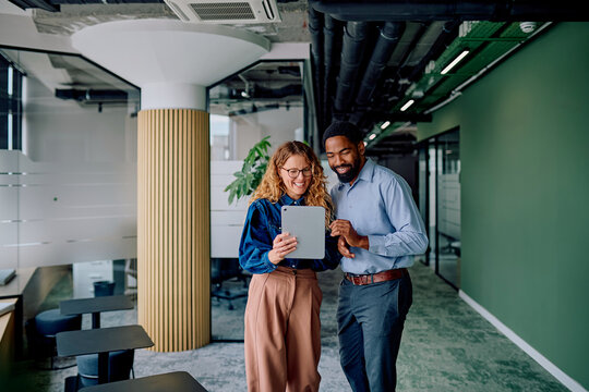 Multiracial business colleagues smiling, discussing digital content on a tablet, fostering teamwork and partnership in a contemporary workspace - Powered by Adobe