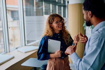 Diverse business professionals having a joyful conversation in a modern office, one holding a digital tablet
