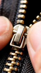 Hand zipping golden zipper on black jacket during garment repair work
