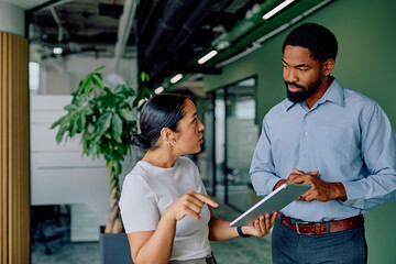 Two diverse business people collaborating, discussing data and new ideas in a modern office using a digital tablet