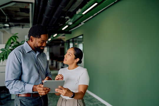 Diverse business professionals collaborating in a modern office, one person showing data on a digital tablet to a colleague
