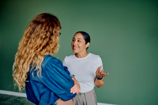 Two women standing together, smiling and talking. They are engaging in a professional discussion or teamwork