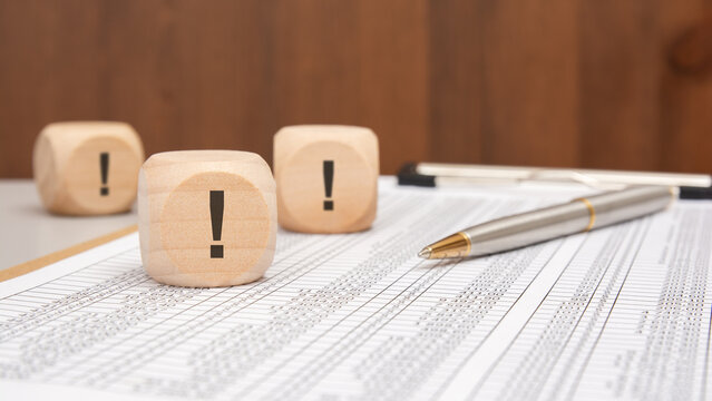 wooden cubes with black exclamation marks on financial spreadsheet with pen and blurred background - Powered by Adobe