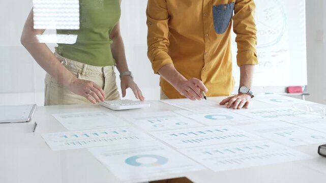 Business professionals analyzing financial reports, pointing at charts during collaborative meeting, discussing data with focused professional demeanor