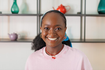 Smiling African woman with dark skin and curly hair poses indoors wearing a pink shirt