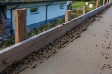 Close up view of a construction site showing a wooden frame with concrete or sand, vertical stakes,...