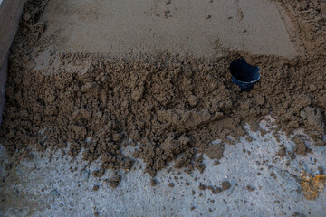 A section of wet concrete with a rough edge meets a smoother surface. A black pipe extends from the concrete, indicating drainage or utility work.