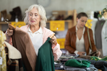 During November sales, senior woman choose and buy warm knitted dress, choose some wardrobe items. Discount season, promotional offers. Chain store of affordable clothing ..