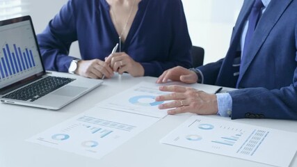 Business colleagues discussing financial data on a laptop and printed documents, analyzing charts and market trends for decisions. Business people and finance concept - Powered by Adobe