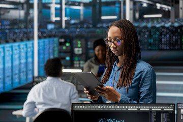 Data center admin using tablet to monitor system performance, identifying bottlenecks. Woman in...