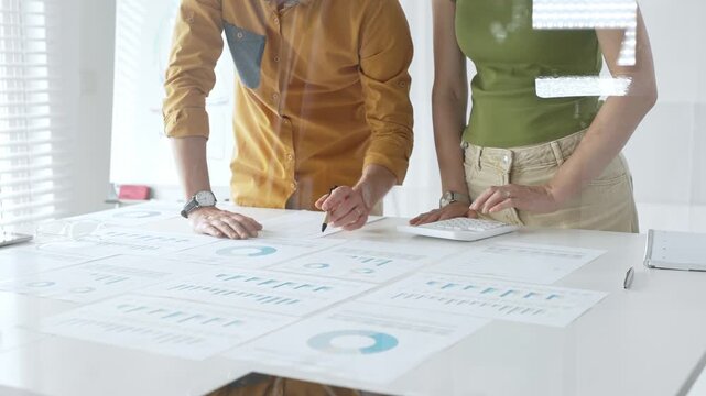 Business professionals analyzing financial reports, pointing at charts during collaborative meeting, discussing data with focused professional demeanor