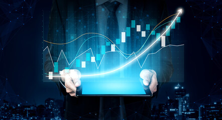 A businessman holds a tablet displaying dynamic financial graphs and data overlays, symbolizing growth and technology in an urban setting at night. Impute