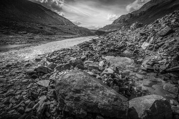 Black and white view of crystal clear pond, in the middle of moraines near a turbid glacial stream. Vallelunga, Alto Adige, Italy