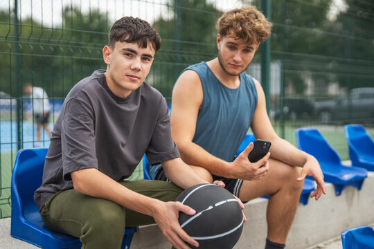 Young men friends resting on bleachers after basketball game