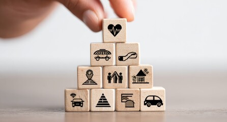 Wooden blocks stacked in a pyramid shape, each displaying a different icon representing various aspects of life. A hand is placing another block on top
