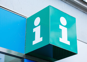 Green information sign with white lettering on a blue building exterior, providing clear guidance for visitors in urban environment