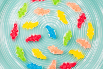 Colorful gummy candy alligator sweets arranged in circular motion on turquoise plate, vibrant jelly candies in red, green, yellow, blue, and orange, playful background for fun food and dessert concept