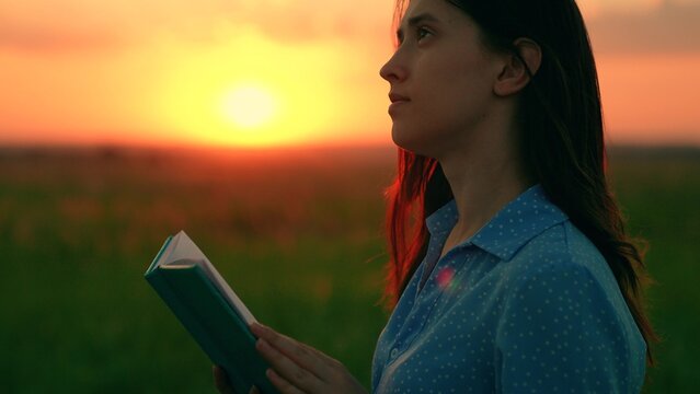 Student reading textbook outdoors in spring. Young woman reading book in autumn park in rays setting sun. Prayer in nature. Man reading book outdoors. Study, education. Beautiful woman praying sunset