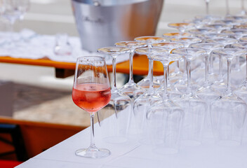 Elegant glass of rose wine stands out among a row of empty wine glasses on a table, showcasing a vibrant outdoor event atmosphere