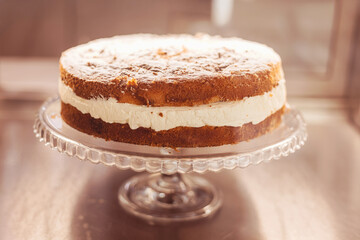 Delicious layered cake on a glass stand in a warm bakery setting at midday invites indulgence and enjoyment