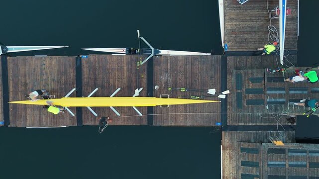 Top View Of Rowing Boat Crews Disembarking After Training. They Carry Rowboats And Oars, Showing Teamwork, Strength, And Post-Workout Routine On The Pier In Halifax Bay.