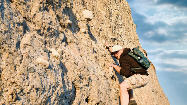 Man rock climbing on steep cliff wall during outdoor adventure sport and extreme activity, person in nature background