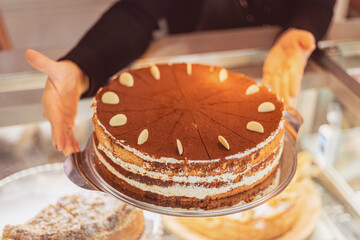Delicious layered cake with almonds showcased by bakery staff in warm afternoon light