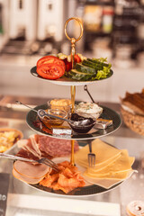 Multi-tiered platter of meats, cheeses, and fresh vegetables in a stylish cafe setting for a savory snack or meal experience
