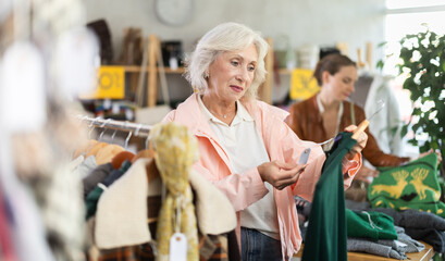 Obraz premium Elderly woman buyer choosing warm dress in clothing store