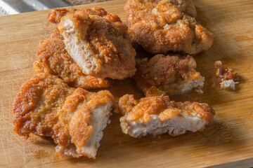 Breaded chicken with a piece cut in half, on a wooden cutting board, close-up photo