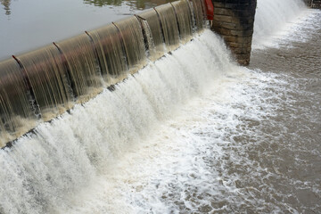 Powerful concrete weir dam with cascading white foam waterfall and turbulent water flow creating...