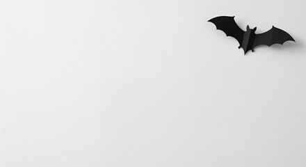 A clean, minimalist composition features a single black paper bat with subtle shadows positioned in the upper right corner against a bright white background.