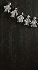 A string of small white fabric ghost figures with black eyes and mouths hangs diagonally across a dark wooden background, offering ample copy space.