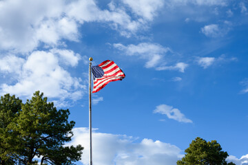 Celebrate independence day, 4th of July, with American flag flying against a sunny blue sky with white puffy clouds, Grand Canyon National Park, Arizona
