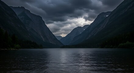 Dramatic mountain landscape with lake reflecting cloudy sky and dark silhouettes
