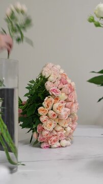 The florist takes a pink Christie bush rose from a vase and forms a bouquet