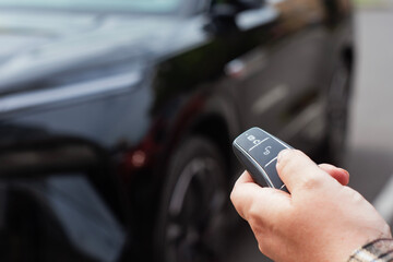 Close-up of a person holding a car key with a remote control in front of an open vehicle door. Concept automotive access, smart keys, car security and modern transportation.