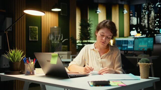 Businesswoman makes mistake in transcribing finance updates on notebook, tearing up the paper sheet and restarting. Discontent impatient worker wanting to finish tasks for the night. Camera A.