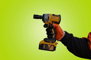 A worker in a protective vest and gloves presses an impact wrench against light green background.
