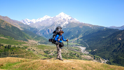 Fototapeta premium Hiker stands proudly on a mountain summit with snow-capped peaks in the background