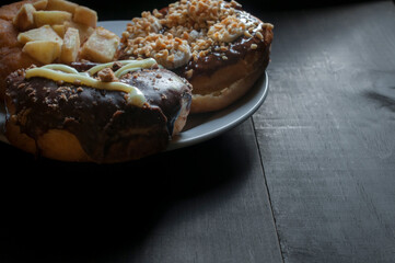 surtido de donas glaseadas en un plato blanco sobre una vieja mesa de madera con luz tenue y a contraluz. Copy space