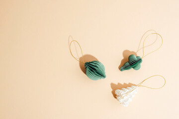 Green and white paper christmas ornaments with golden strings on beige background. Festive flat lay, top view, copy space