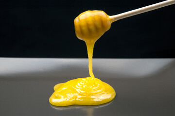 Honey is drizzled from a wooden stick, pooling in a bright yellow puddle on a smooth surface