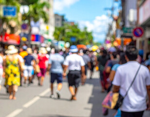 Blurred, defocused crowd of unrecognizable people walking down a busy street lined with shops and tropical greenery under a sunny blue sky. Captures the vibrant atmosphere of a summer street festival 