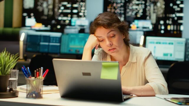 Business director sleepy and burdened at the office late at night, experiencing workplace challenges and anxiety. Discouraged woman struggling with intense workload after hours. Camera A.