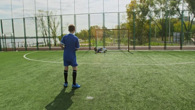 Back view shot of unrecognizable preteen boy performing penalty while goalkeeper defending goal